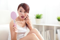 unhappy Woman finding acne on face by mirror at home, asian beauty